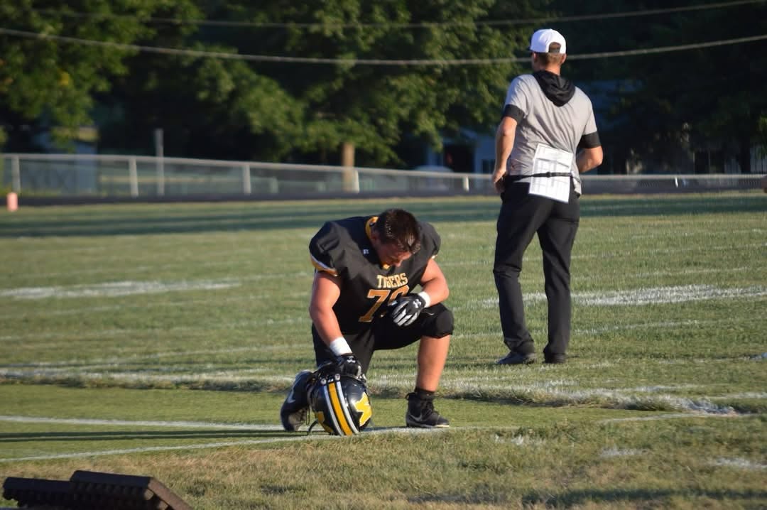 Markos Black kneels beside his helmet before a Marceline Tigers game.