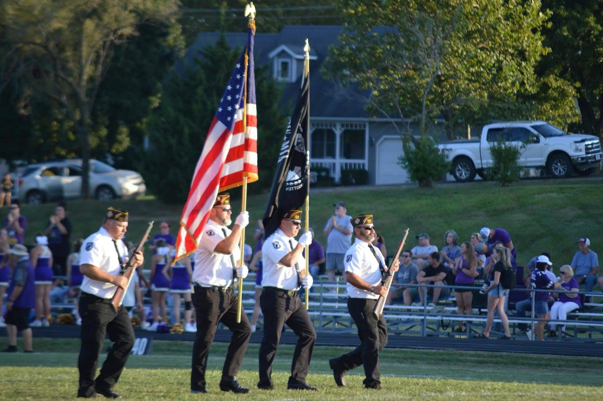 Veterans carry flags across the Marceline football field as the crowd looks on.